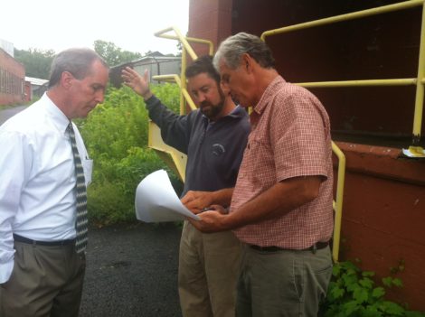 Douglas L. Brown, AIA, shows state Rep. William Smitty Pignatelli and William Powers from Congressman Richard Neal’s office the plans for Smith Mill redevelopment. The narrow street behind them is an obstacle to the site’s development, plans call for demolition of the buildings in the background. Photo: Daniel Bellow