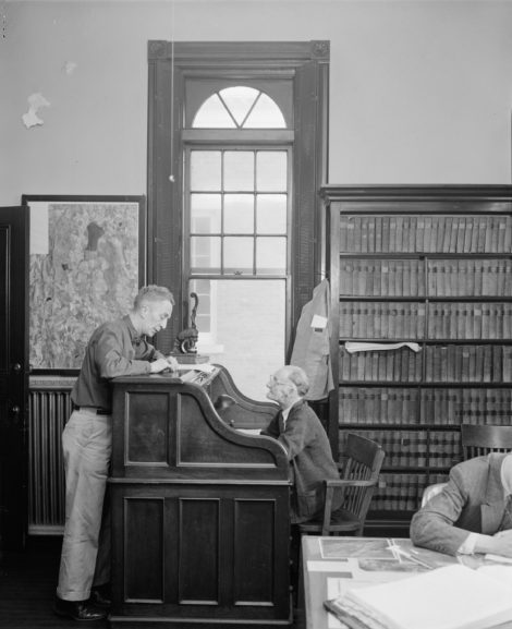 Town Treasurer Graham D. Wilcox Sr. posed while seated at his desk with Norman Rockwell standing in front of it.
