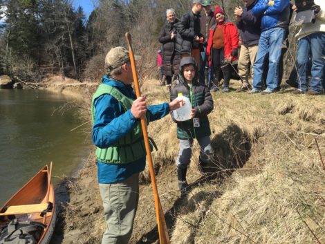 Ten-year-old Isaac Scribner hands the jug of spring water to Denny Alsop to begin the trek.