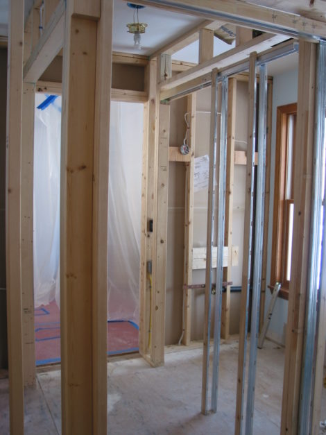 This view during construction looks toward the entry where the plastic hangs. On the right is the framing for the new powder room while the frame for the closet opening is on the left. - Photo Credit: Erica Fay